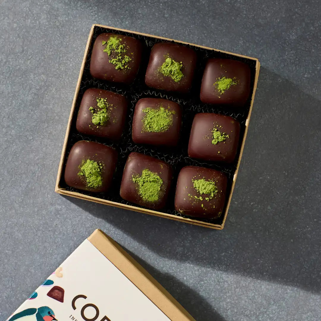 A box of coracao nine matcha fudge truffles with green matcha powder on top, placed on a grey surface with the packaging visible.